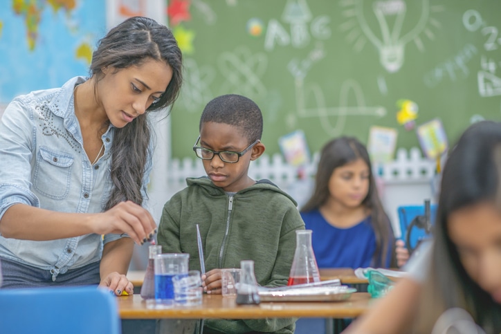 A young female teacher helps a boy in her class to conduct a chemistry experiment.