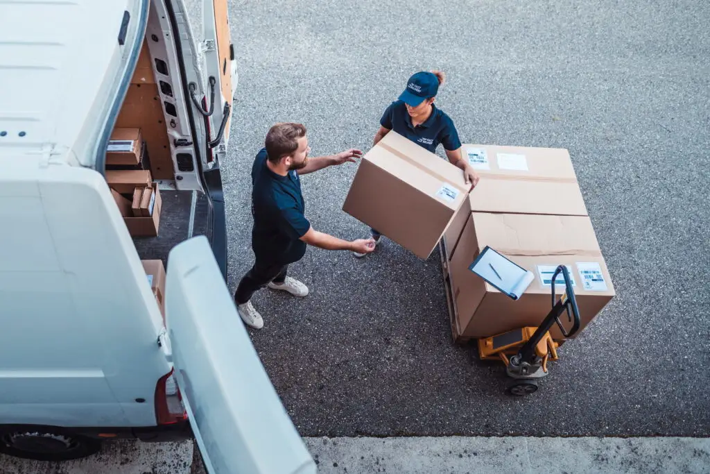 Two delivery workers loading cardboard boxes into a white van.