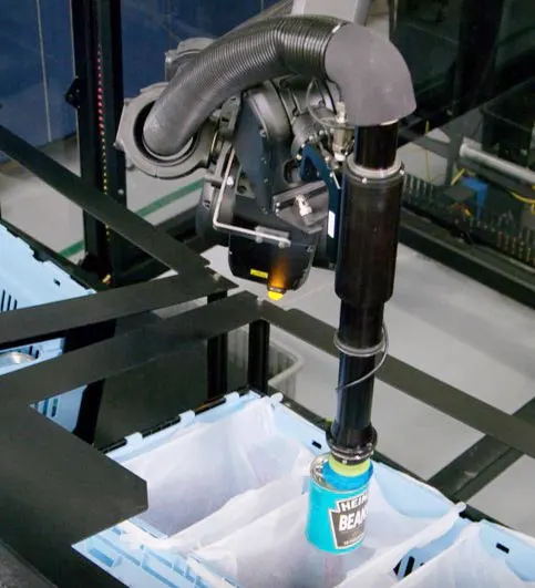 Close-up of a robotic suction arm picking a can of baked beans.