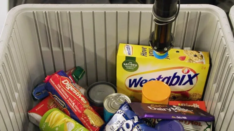 Robotic arm picking items from a bin filled with grocery products.