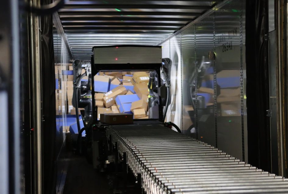 Automated roller conveyor loading stacked cardboard packages inside a truck trailer.