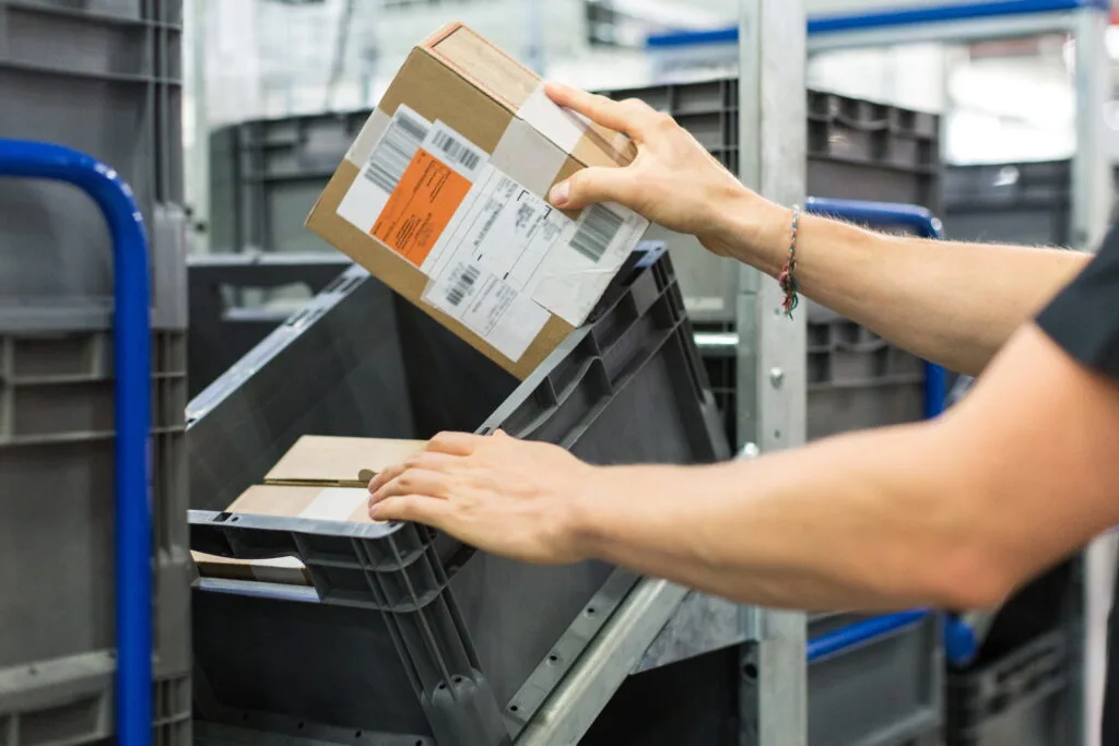 Worker placing a small packaged box into a grey storage bin.