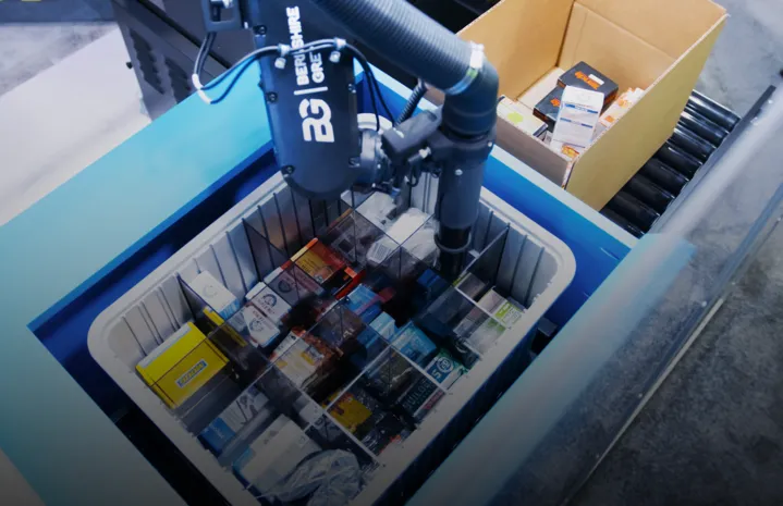 Robotic arm picking items from a cardboard box into a compartment tote.